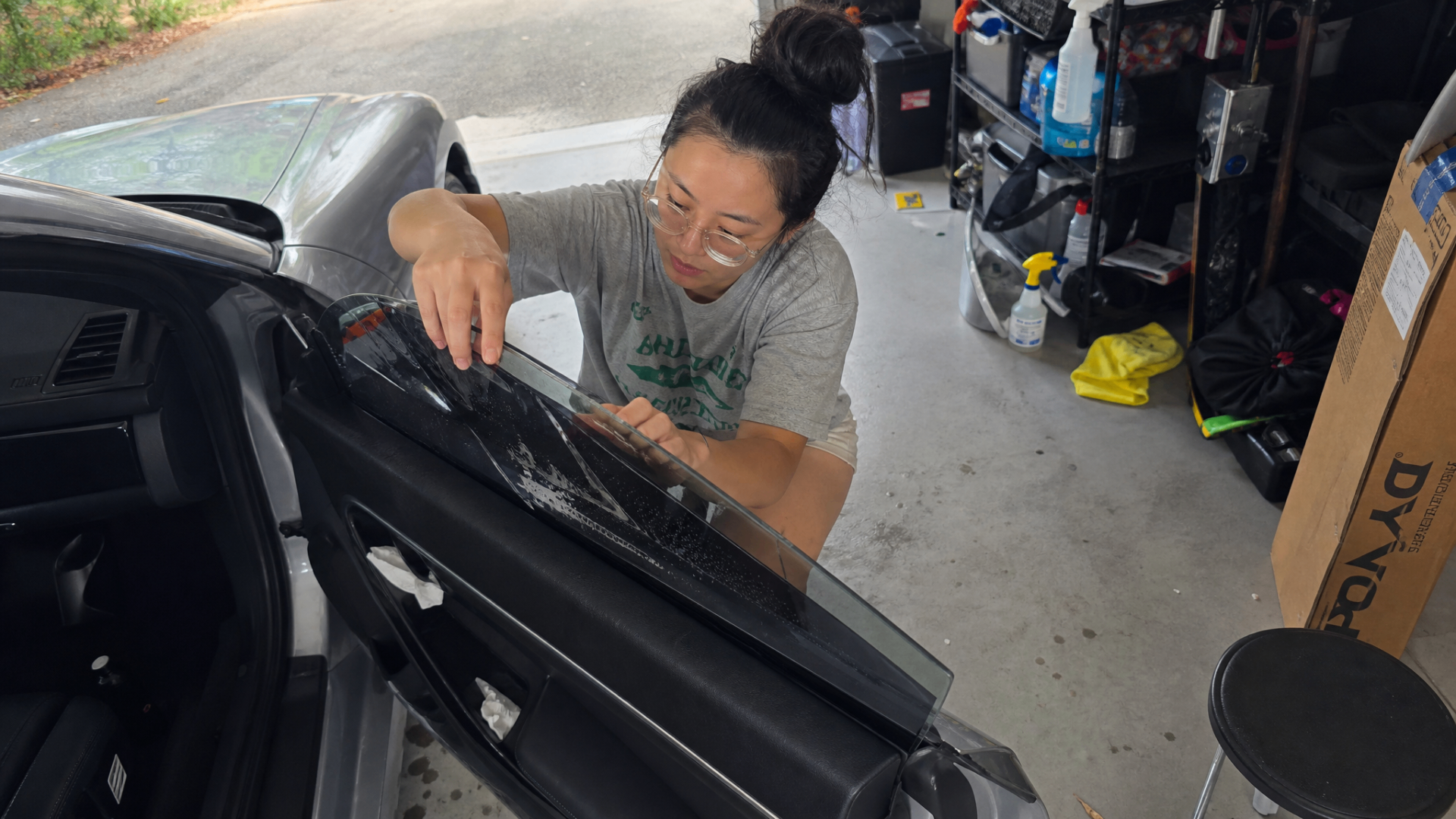 Hannah crouched beside a car door carefully positioning film along the inside glass in her garage.