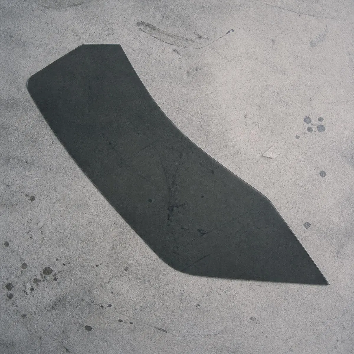 Une seule pièce de film à vitres teintées céramique foncé prédécoupé, posée sur du béton gris.